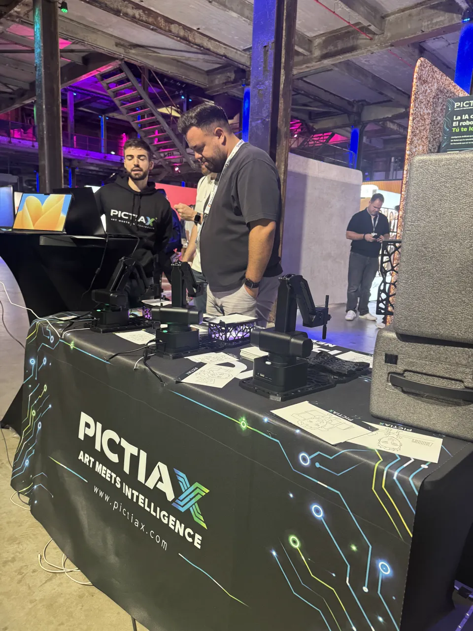 Two people at the PictiaX® booth table, looking at the caricature robots